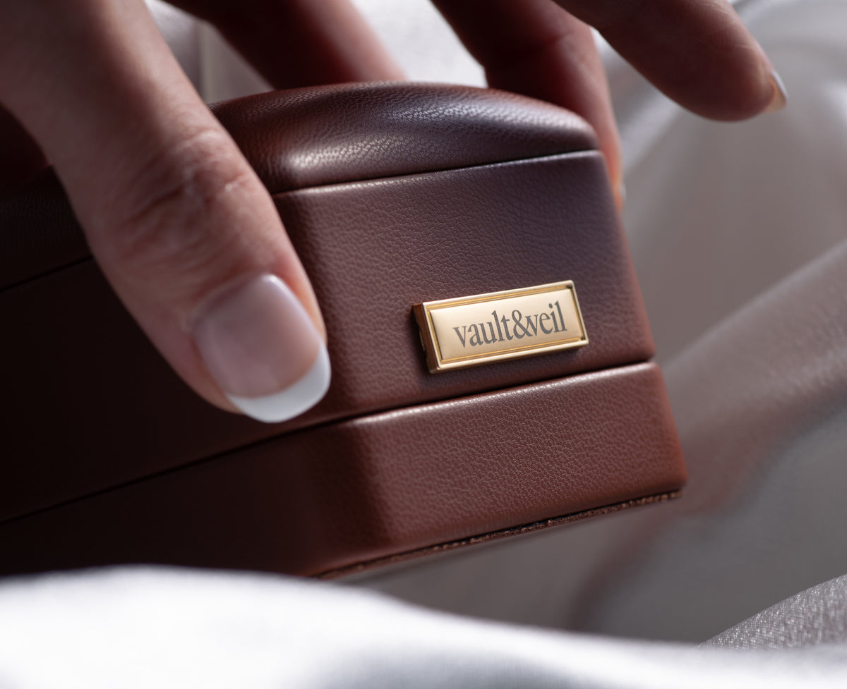 Hand holding a closed Vault & Veil jewelry box against silk fabric.